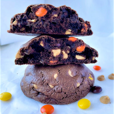 Two warm and gooey chocolate peanut butter chip cookies, each loaded with peanut butter chips and Reese's Pieces. One cookie is broken open to reveal the delicious filling inside.